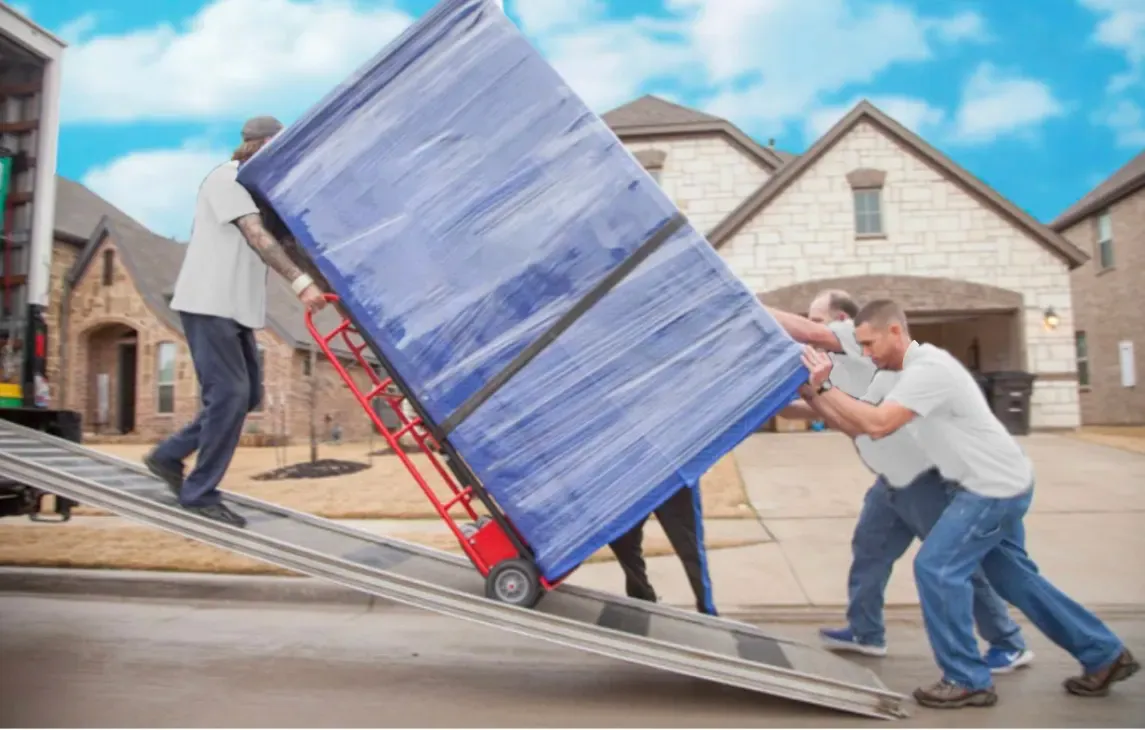 Movers guiding a wrapped dresser on a hand truck